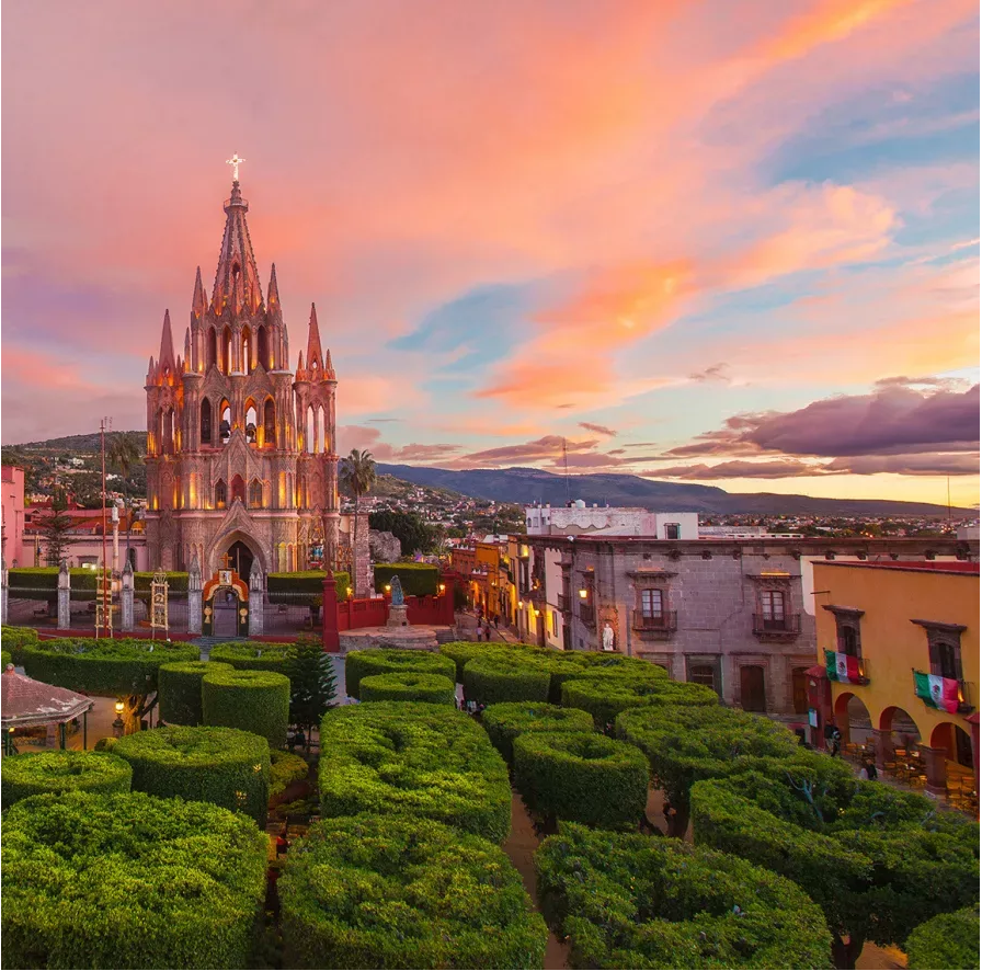 Vista de San Miguel de Allende al atardecer con jardines y la Parroquia